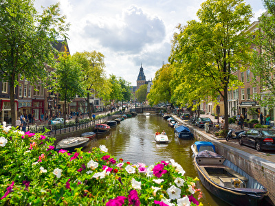 Een schilderachtig kanaal in het centrum Amsterdam met meerdere boten langs de kant en witte en roze bloemen op de voorgrond 